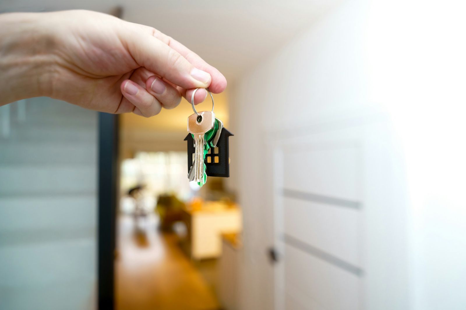 Hand hält einen Hausschlüssel vor einer Wohnungstür